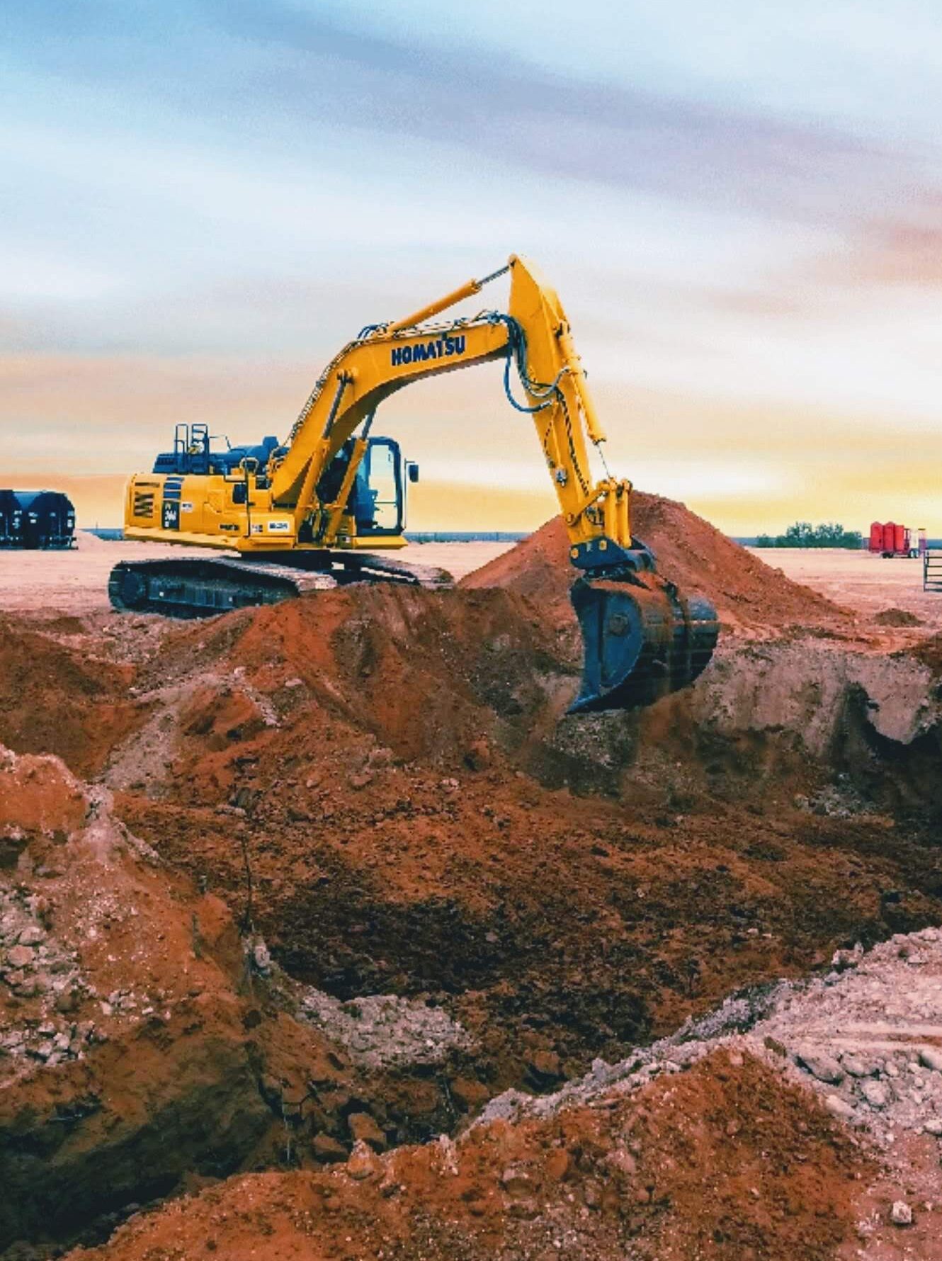 Excavator Digging and Moving Red Soil on a Construction Site During Sunset